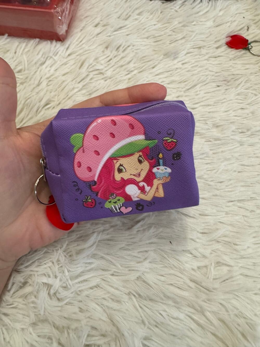 Purple Strawberry Shortcake mini pouch holding a cupcake charm keychain